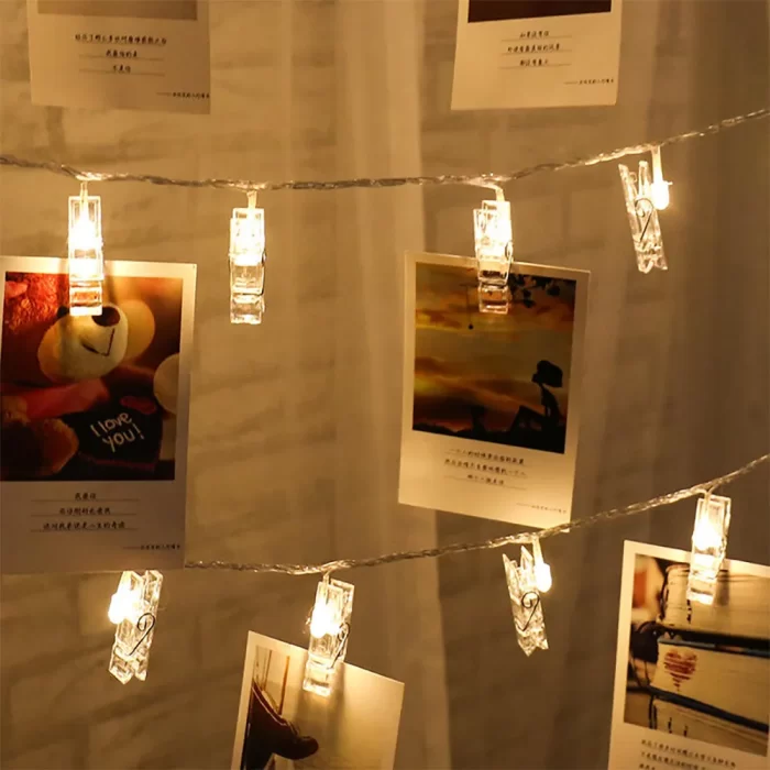 Warm string lights with transparent photo clips gently illuminate a cozy bedroom, hanging cherished photos above the bed to create a dreamy, personalized retreat.