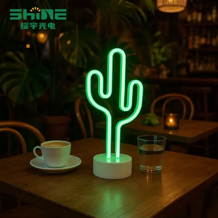 Green cactus LED desk lamp glowing beside laptop, notebook and coffee mug in cozy workspace