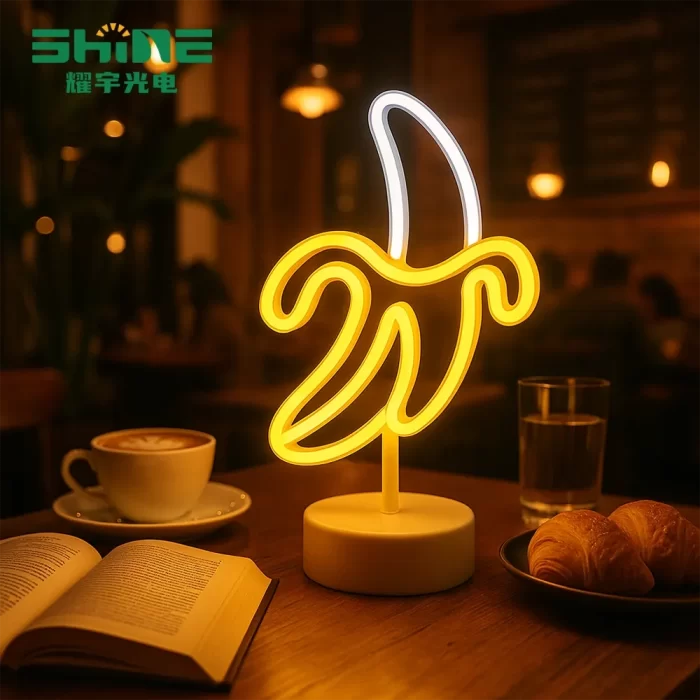 Banana-shaped LED lamp glowing with golden light on a café table, beside coffee and books, creating a cozy atmosphere that attracts customers and enhances hotel or café brand image