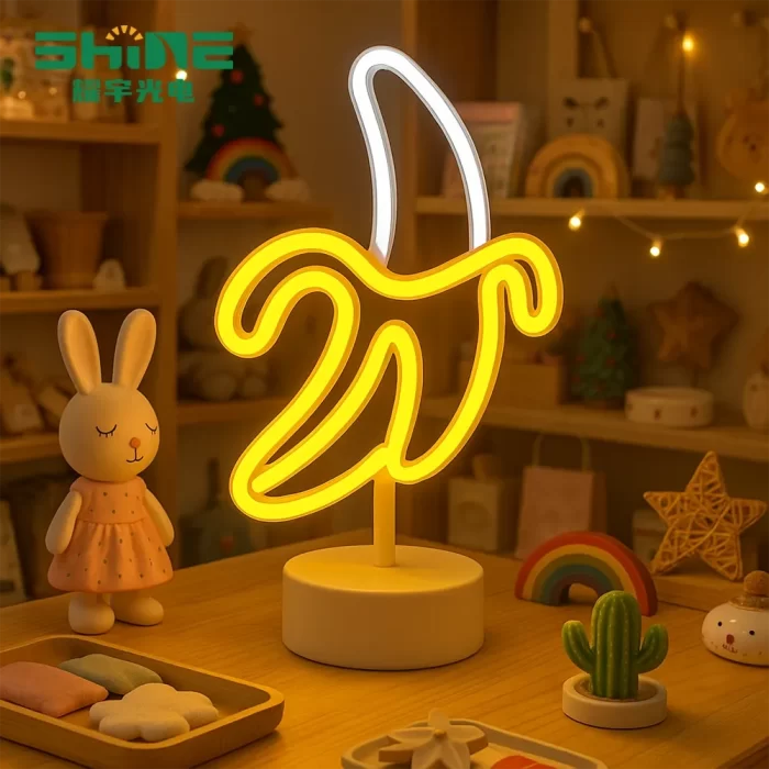 Playful banana-shaped LED lamp glowing warmly on a desk in a gift shop, surrounded by toys, rainbow decor, and cactus ornament, ideal as a household decoration or gift product