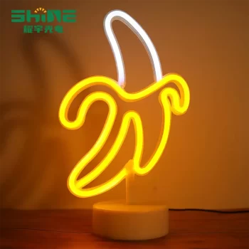 playful banana-shaped neon lamp with warm golden glow on a desk, surrounded by flowers and decorative items, perfect for home or bedroom decor