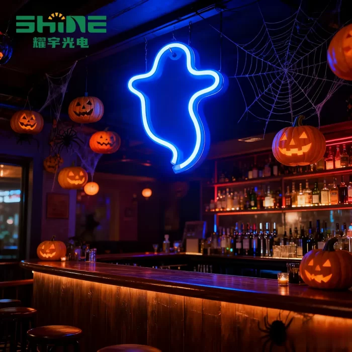Blue holiday neon sign shaped like ghost highlights Halloween bar section, separating counter area with pumpkins and cobweb décor.