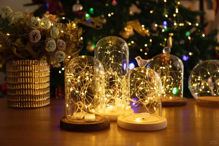 Glass cloches filled with warm white LED fairy lights on a wooden table; Christmas tree bokeh in the background.