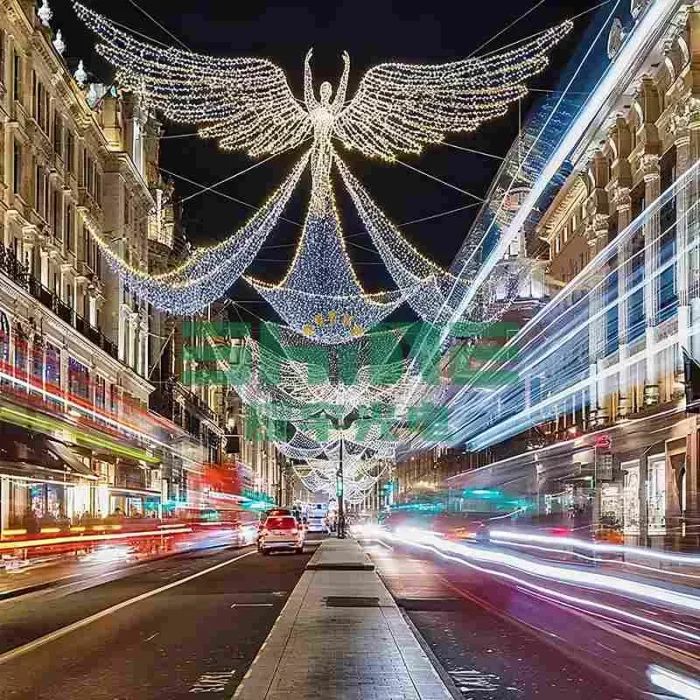 A magnificent 2D angel lighting motif with large, illuminated wings suspended over a busy city street at night, creating a magical Christmas holiday display.