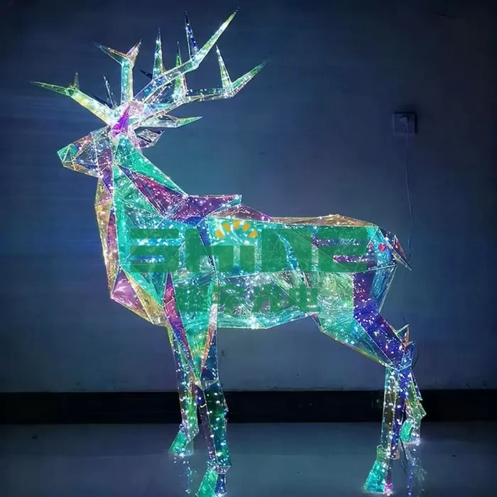 Colorful 3D LED light display of a deer sculpture with glowing multicolored lights, creating a vibrant and festive atmosphere. The deer is crafted with angular geometric shapes.
