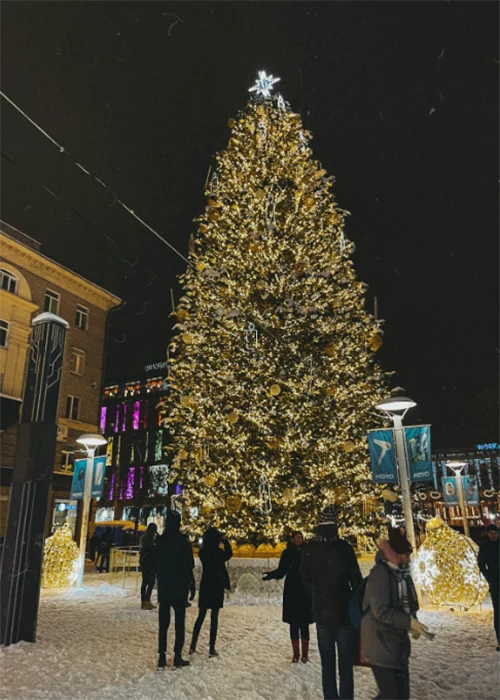 Tall 3D LED motif Christmas tree covered in warm white lights in a downtown square with people standing around it, representing a large municipal holiday lighting project