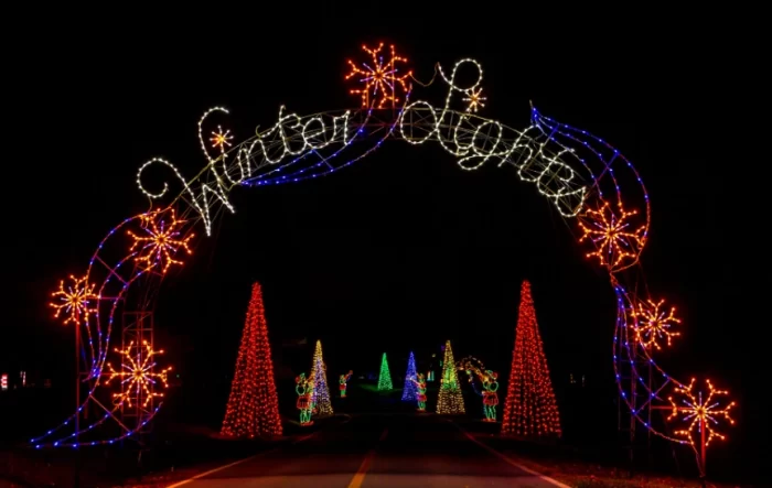 Drive-through Winter Lights entrance arch made from 3D motif lights over a roadway, with cone-shaped light trees behind, demonstrating structural and environmental engineering needs.