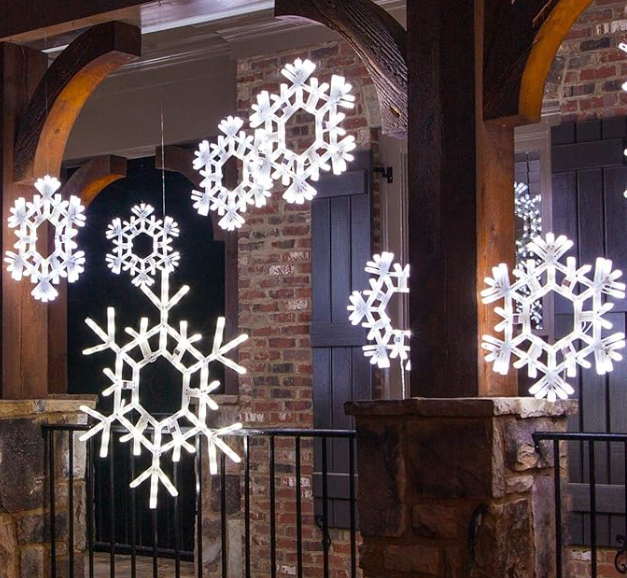 Multiple bright white LED snowflake motif lights hanging from a covered front porch in front of a brick house