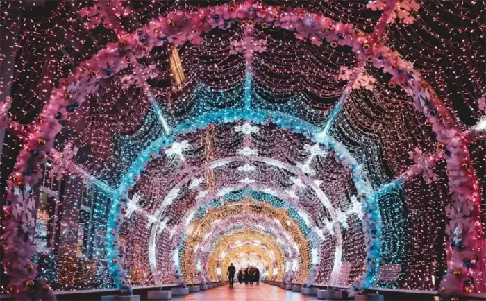 People walking through an interactive 3D LED motif light tunnel with colorful arches