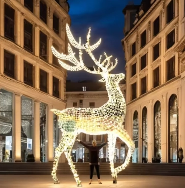 Massive illuminated reindeer motif Christmas lights sculpture in a city square with a person standing beneath it for scale.