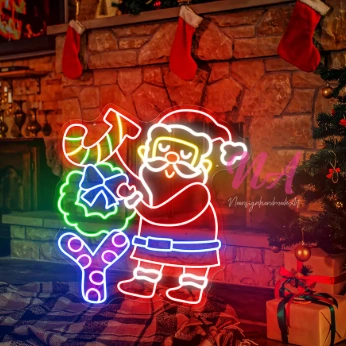 Colorful neon flex Santa motif Christmas lights with a JOY sign and wreath glowing beside a cozy Christmas fireplace.