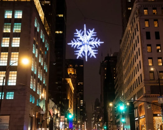 Huge LED snowflake motif Christmas lights suspended above a downtown street, creating dramatic holiday impact at night.