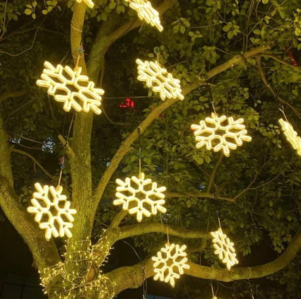 Glowing warm white snowflake motif Christmas lights hanging from the branches of a tree to highlight the garden at night.