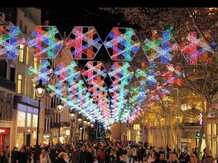Colorful geometric RGB LED canopy motifs spanning a busy pedestrian shopping street at night.
