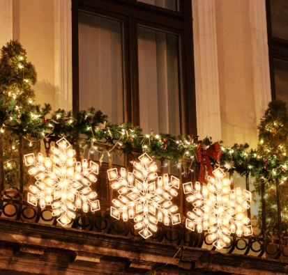Illuminated snowflakes on a balcony railing, decorated with garlands for a cozy Christmas atmosphere.