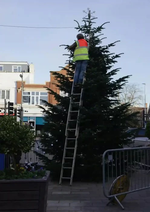 Contractor installing a large commercial lighting motif display using a ladder at night
