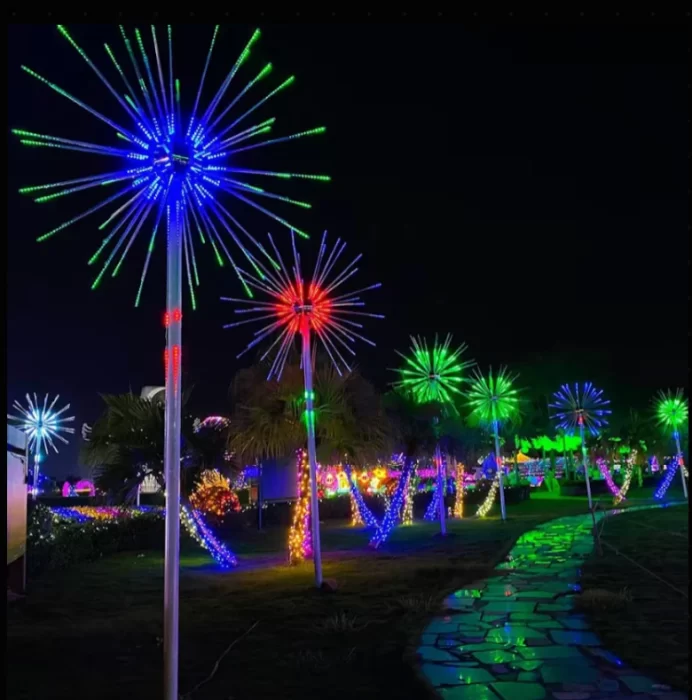 Multiple RGB LED firework lights synchronized along a landscaped park path, showing blue, green and red starburst effects for large outdoor displays.